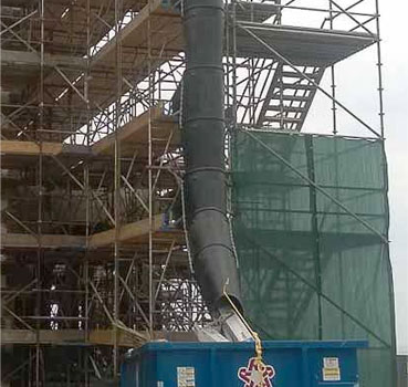 External chute on a construction site feeds a dumpster on the ground
